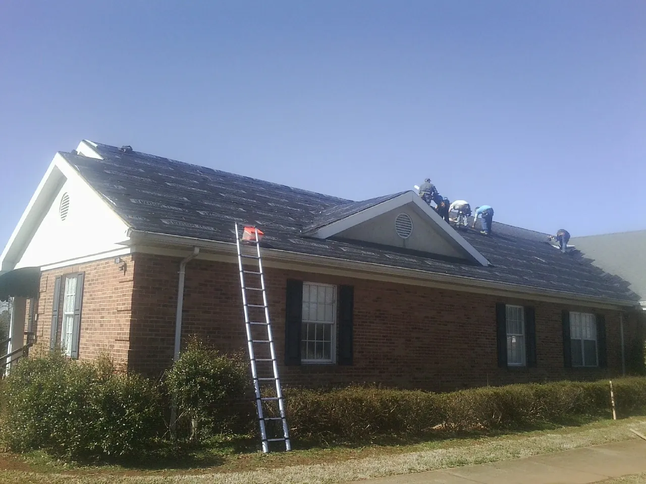 Crew tearing shingles off a brick ranch roof with a ladder set — Metal Roof Repair work by our crew in Morton