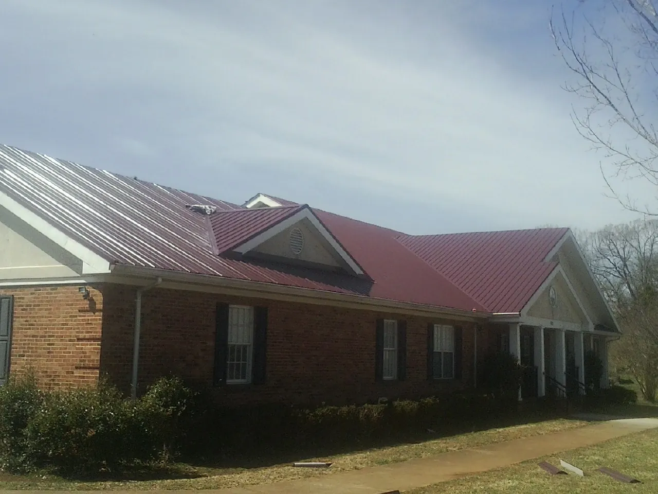 Red metal roof with gabled entries on a long brick building, from a Hail Damage Roof Repair job in Morton