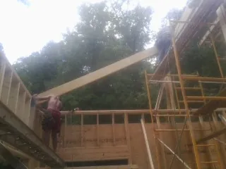 Carpenter raising a rafter beam on a new second story frame in Morton